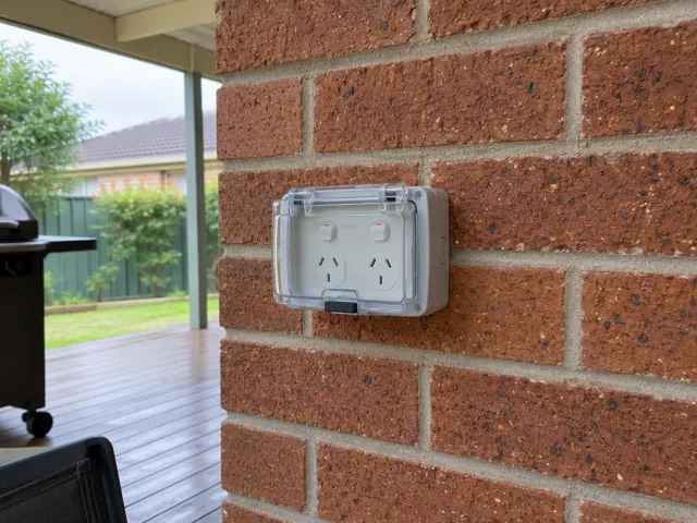 Outdoor double power point with weatherproof cover on a brick house wall under a covered patio in Cardiff
